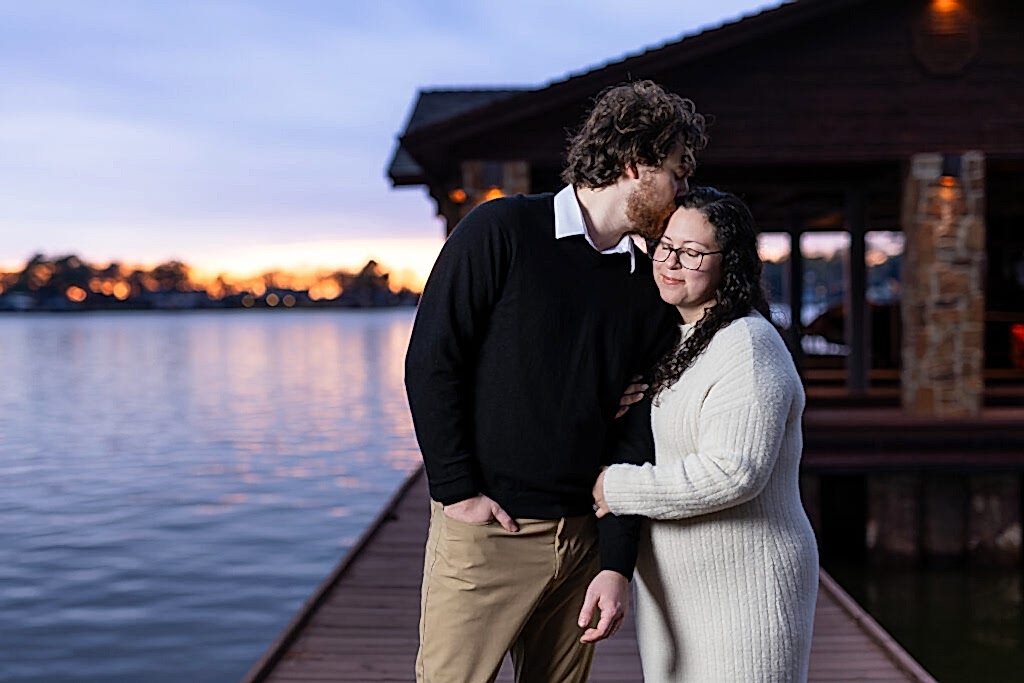 Engaged man kissing fiancée on forehead on boat dock at sunset during Mabank lakehouse engagement session