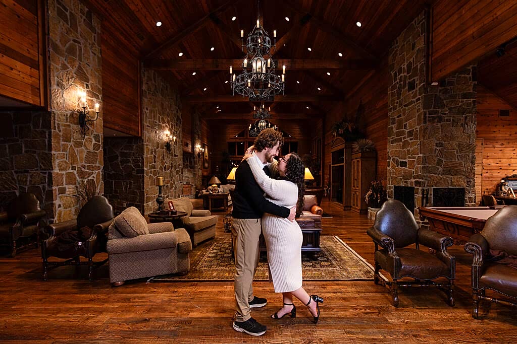 Couple standing facing eachother and smiling inside main living space in lake house for engagement session in North Texas