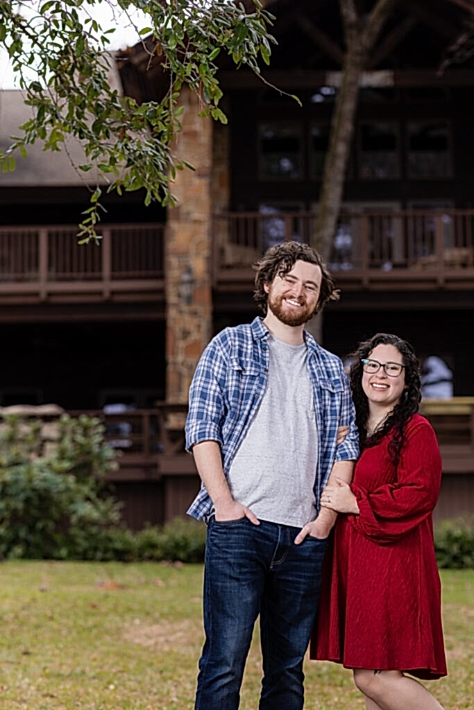 Engaged couple standing together in front of lakehouse smiling during engagement session in Mabank