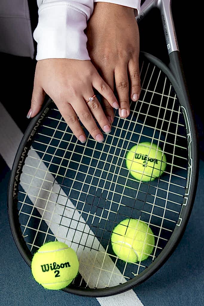 Close up photo of hands on tennis racket showing off heart engagement ring