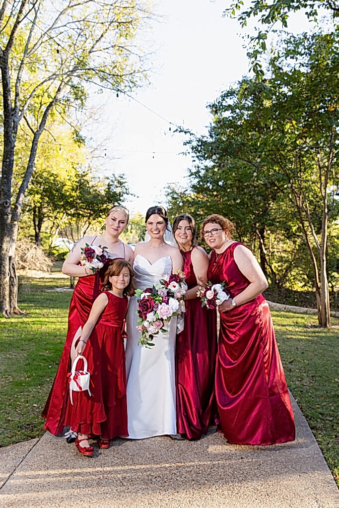Bride and bridesmaids wearing red in the woods at Bella Woods wedding and event venue in Midlothian TX