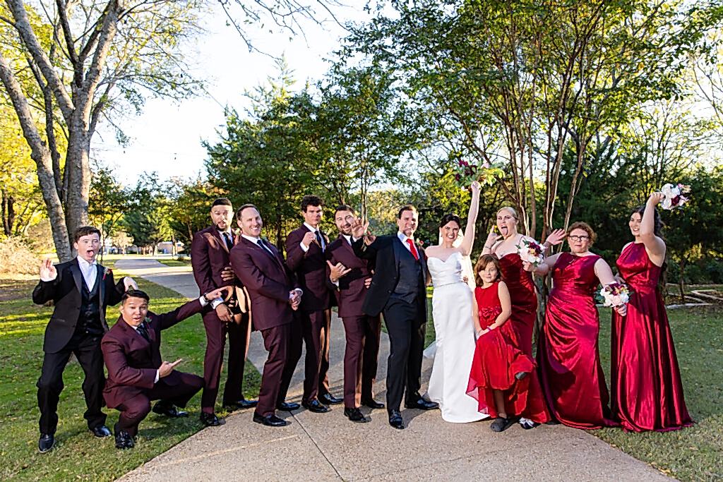 Fun wedding party cheering and wearing red and maroon in the woods at Bella Woods wedding and event venue in Midlothian Texas