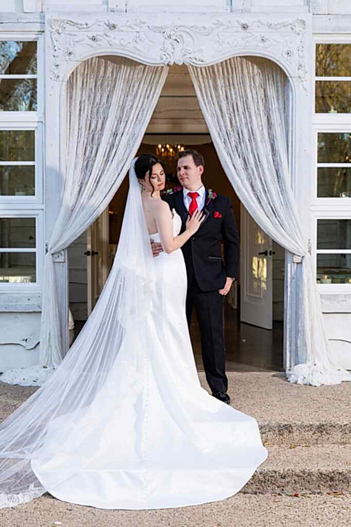Bride with long veil and groom standing in doorway of white Chandler Chapel at Bella Woods