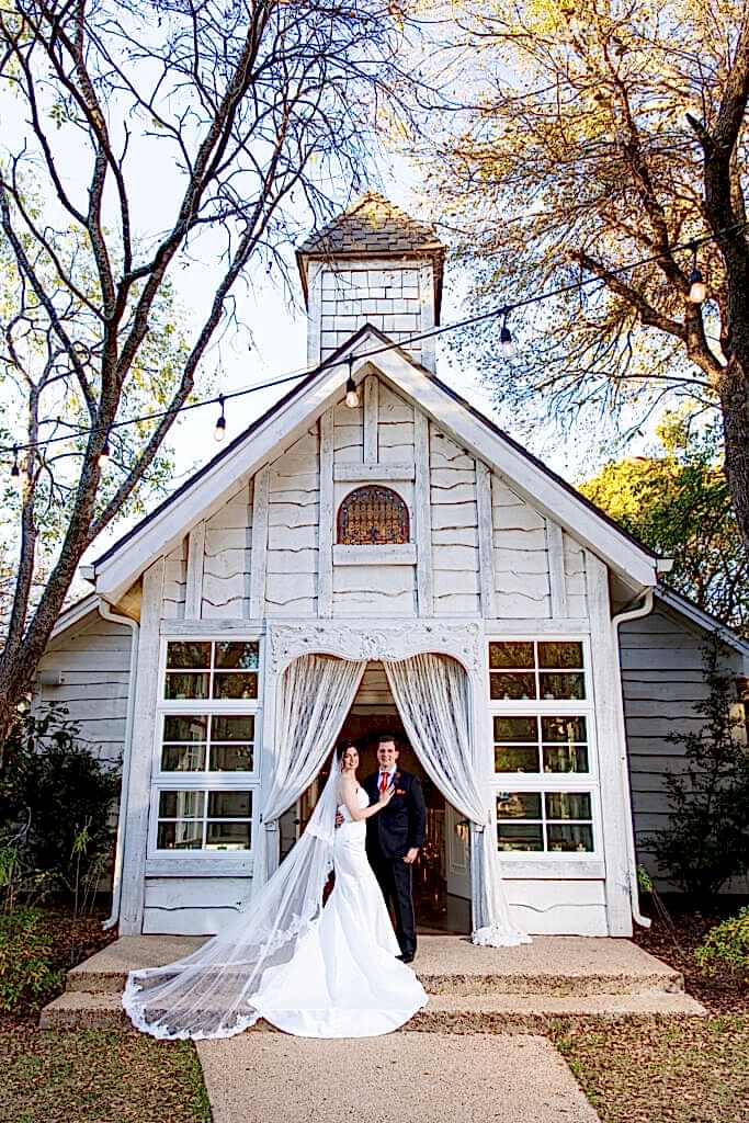 Bride with flying veil and groom standing in doorway of Chandler Chapel at Bella Woods wedding venue in Midlothian Texas in the woods