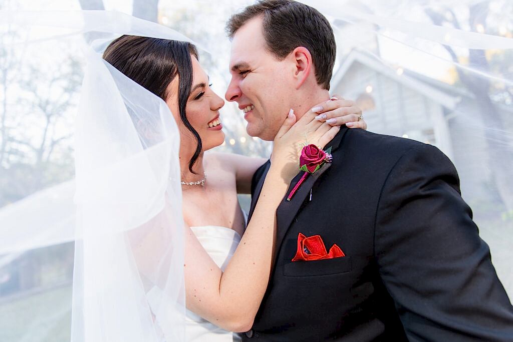 Bride with flying veil hanging on to groom while laughing
